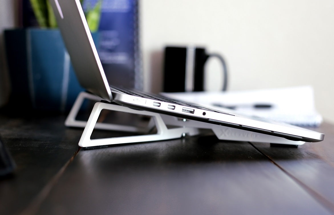 FlexVerk Laptop Stand in Pearl White shown supporting an open Macbook Pro on a wooden desk with a plant and coffee cup in the background.
