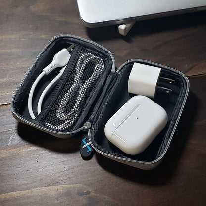 The FlexVerk hard shell protector case shown open on a wood table. Inside there is an airpods case, a USB cable, and a USB wall charger.